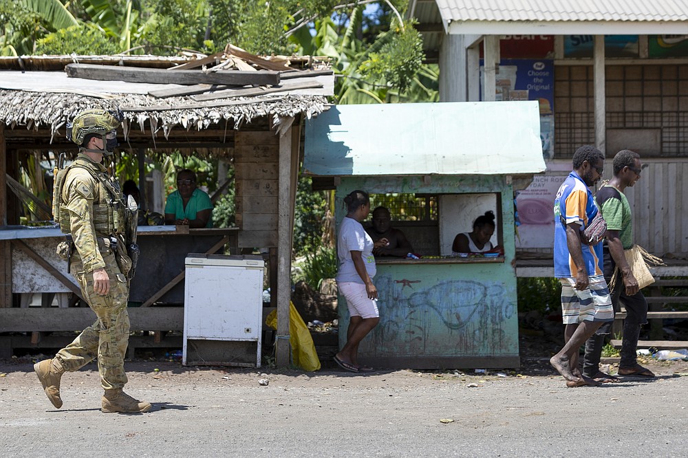 In this photo provided by the Department of Defence, Australian Army Corporal Aaron Woodham walks during a community engagement patrol through Honiara, Solomon Islands, Saturday, Nov. 27, 2021. Solomon Islands police have found multiple bodies in a burned-out building and arrested more than 100 people in this week's violence sparked by concerns about the Pacific nation's increasing links with China. (Cpl. Brandon Grey/Department of Defence via AP)