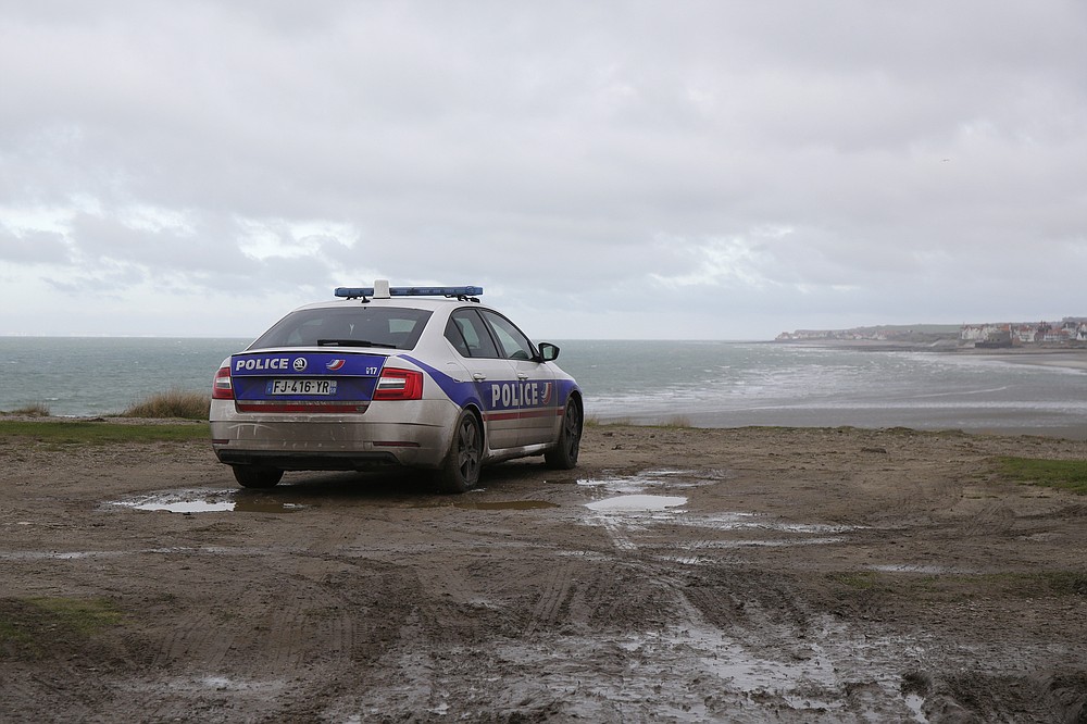 FILE- A police car parks over the shore in Wimereux, northern France, Thursday, Nov. 25, 2021 in Calais, northern France. The price to cross the English Channel varies according to the network of smugglers, between 3,000 and 7,000 euros. Often, the fee also includes a very short-term tent rental in the windy dunes of northern France and food cooked over fires that sputter in the rain that falls for more than half the month of November in the Calais region. (AP Photo/Michel Spingler, File)