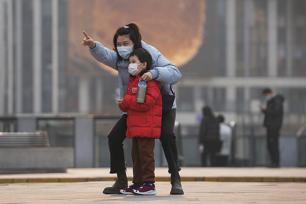 A woman and a child, both wearing face masks to protect from COVID-19 look at a commercial office building in Beijing, Sunday, Nov. 28, 2021. (AP Photo/Andy Wong)