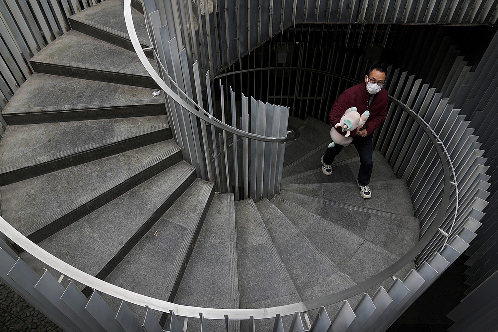 A man wearing a face mask to protect from COVID-19 holds a unicorn soft toy as he walks up an oval staircase at a commercial office building in Beijing, Sunday, Nov. 28, 2021. (AP Photo/Andy Wong)