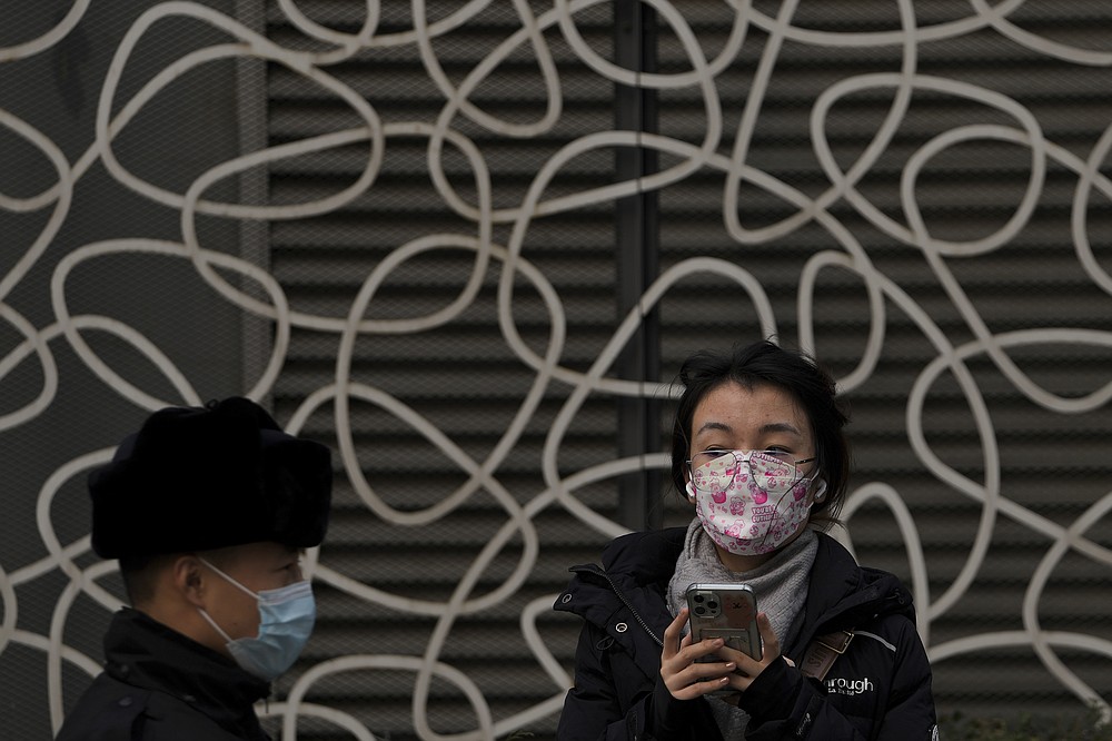 A woman wearing a face mask to protect from COVID-19 looks at a masked security guard patrolling at a commercial office building in Beijing, Sunday, Nov. 28, 2021. (AP Photo/Andy Wong)