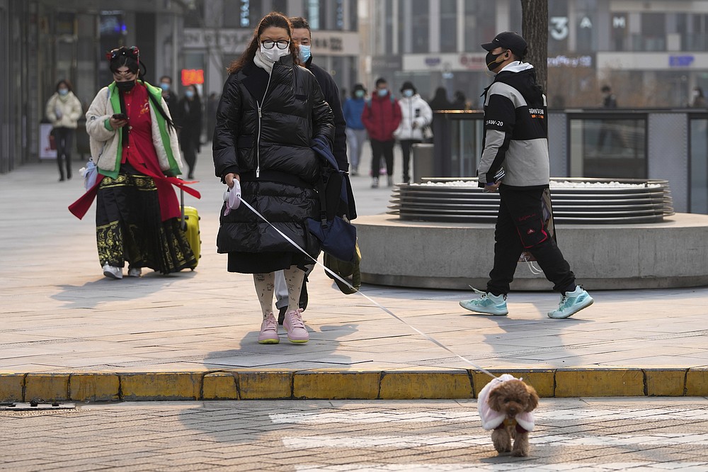 A woman wearing a face mask to protect from COVID-19 walks a dog at a commercial office building in Beijing, Sunday, Nov. 28, 2021. (AP Photo/Andy Wong)