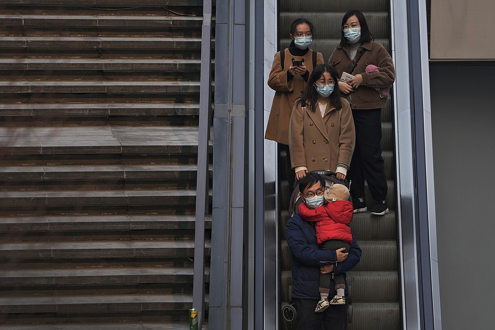 People wearing face masks to protect from COVID-19 take an escalator at a commercial office building in Beijing, Sunday, Nov. 28, 2021. (AP Photo/Andy Wong)