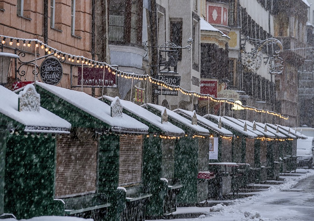 Christmas booths are all closed on the Christmas market in Innsbruck, Austria, as snow falls on Sunday, Nov. 28, 2021. Austria is in a lockdown following a spike in COVID-19 infections. (AP Photo/Michael Probst)