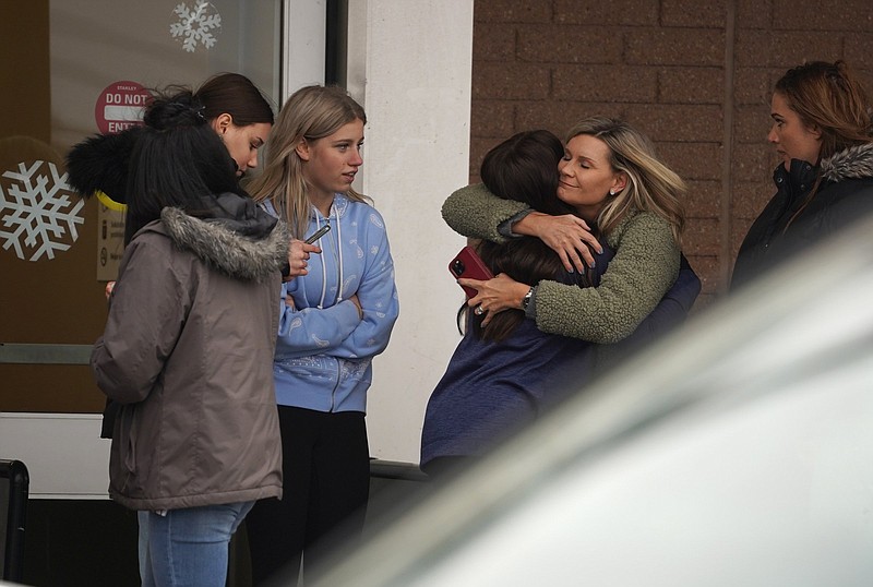 A parent hugs a child as others come to pick up students from the Meijer store in Oxford, Mich., following an active shooter situation at Oxford High School, Tuesday, Nov. 30, 2021. Police took a suspected shooter into custody and there were multiple victims, the Oakland County Sheriff's office said. (Ryan Garza/Detroit Free Press via AP)