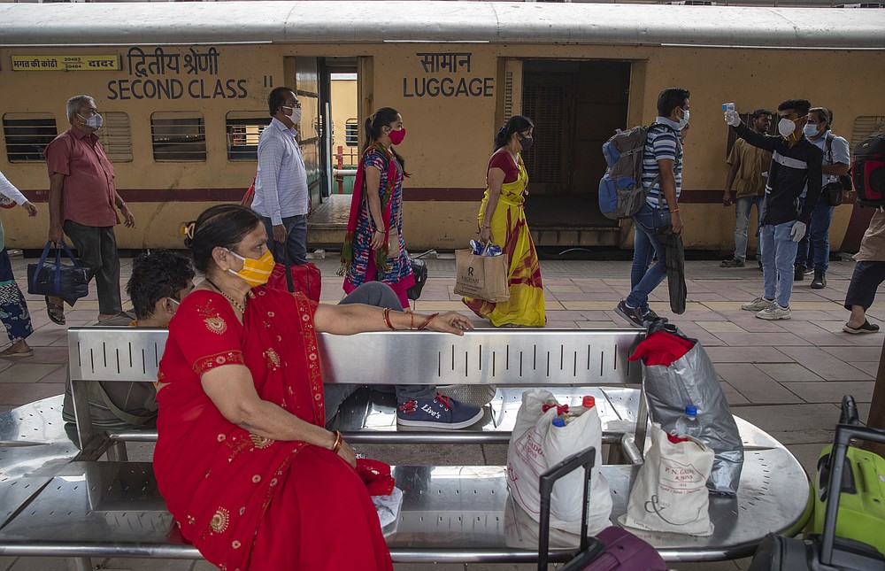 A health worker checks the body temperature of travelers as a precaution against the coronavirus before allowing them to proceed at train station in Mumbai, India, Tuesday, Nov. 30, 2021. (AP Photo/Rafiq Maqbool)
