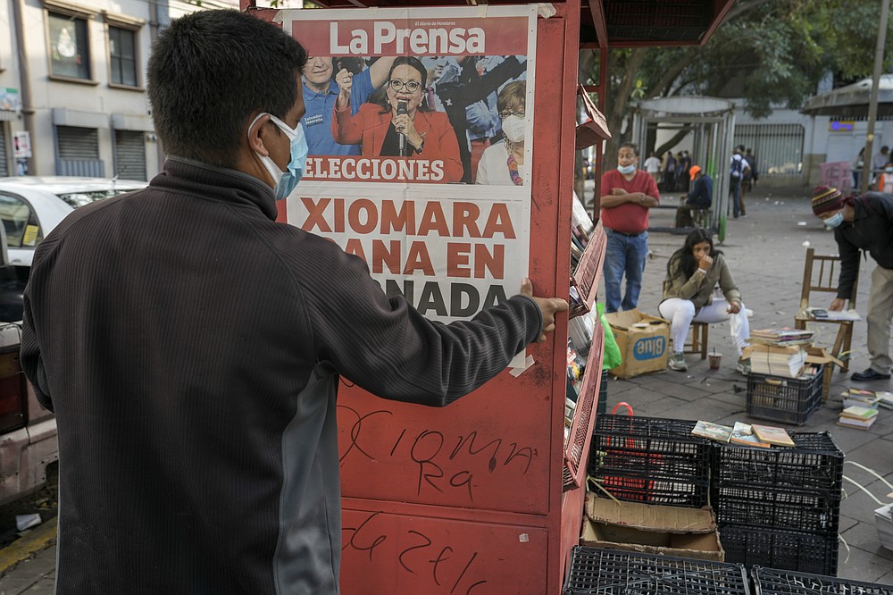 A man sets up his newspaper stand by hanging a poster with a photo of Free Party presidential candidate Xiomara Castro and the day&amp;#xb4;s headline of her expected victory, after general elections in Tegucigalpa, Honduras, Monday, Nov. 29, 2021. Castro is holding a commanding lead as Hondurans appear poised to remove the conservative National Party after 12 years of continuous rule. (AP Photo/Moises Castillo)