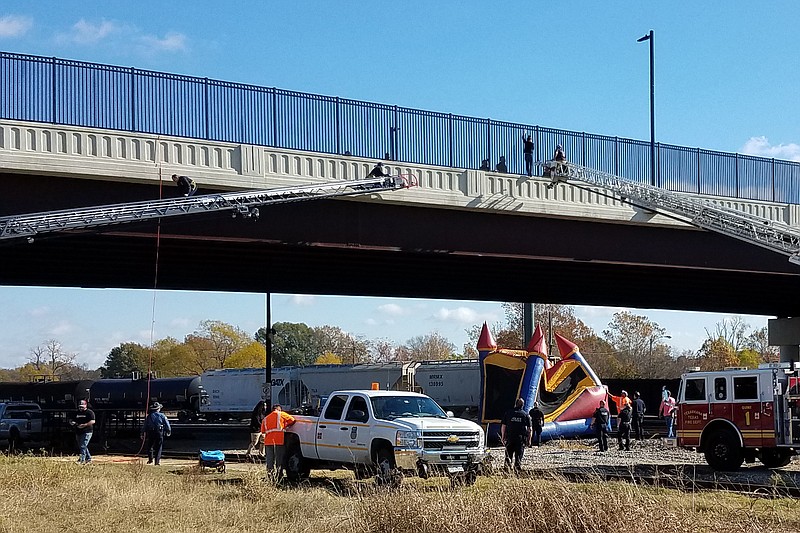 Responders position an inflated children's bounce castle beneath a woman threatening to jump from an overpass Wednesday in Texarkana, Arkansas. As she moved first toward one fire engine ladder and then the other, a crew on the ground moved the bounce castle back and forth to keep it beneath her. The incident ended when a Texarkana Texas Fire Department firefighter manning the ladder on the right put his arms around her waist and held on as she was lowered to the ground. She was taken into custody apparently unharmed. (Staff photo by Karl Richter)