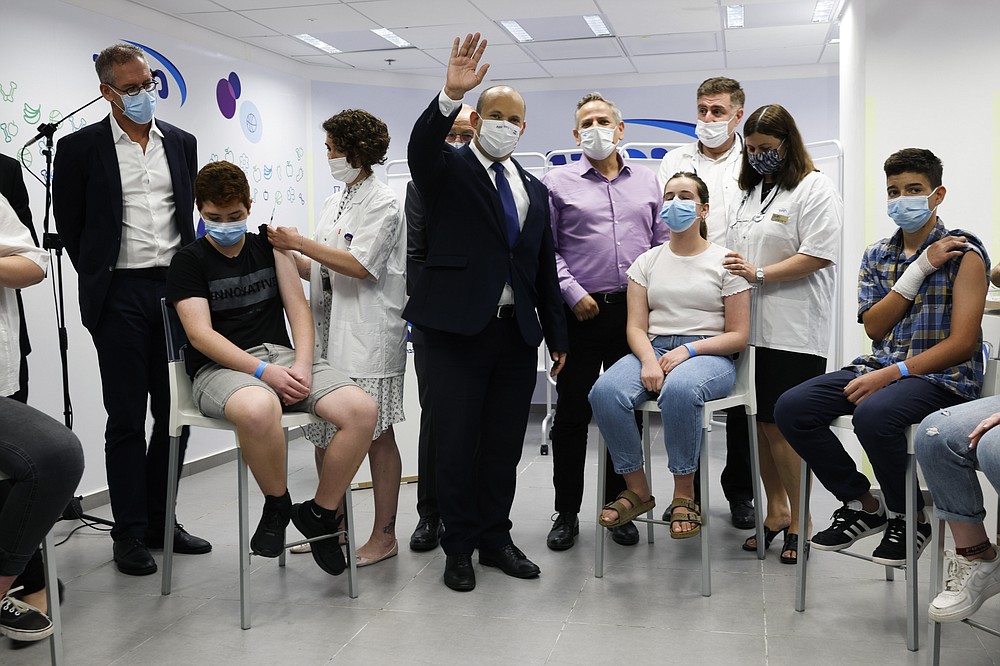 FILE - Israeli Prime Minister Naftali Bennett, center, gestures as he stands next to youths during his visit to a Maccabi healthcare maintenance organisation (HMO) outlet which offers vaccinations against the coronavirus disease (COVID-19) in Holon, near Tel Aviv, Israel Tuesday, June 29, 2021. The coronavirus&#x27;s omicron variant kept a jittery world off-kilter Wednesday Dec. 1, 2021, as reports of infections linked to the mutant strain cropped up in more parts of the globe, and one official said that the wait for more information on its dangers felt like &amp;#x201c;an eternity.&amp;#x201d; (Amir Cohen/Pool Photo via AP, File)