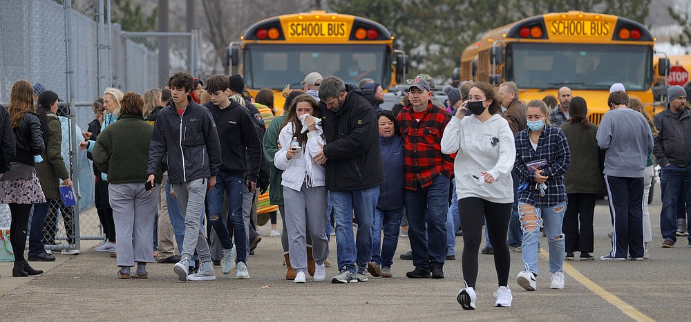 Parents walk away with their kids from the Meijer&#x27;s parking lot, where many students gathered following an active shooter situation at Oxford High School, Tuesday, Nov. 30, 2021, in Oxford, Mich. Police took a suspected shooter into custody and there were multiple victims, the Oakland County Sheriff&#x27;s office said. (Eric Seals/Detroit Free Press via AP)