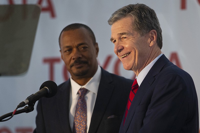 North Carolina Gov. Roy Cooper smiles as Toyota Motor Administrative Officer Chris Reynolds, left, stands with him to celebrate their new partnership during an announcement of the future site of a new Toyota battery manufacturing plant in Liberty, N.C., Monday, Dec. 6, 2021. (Kenneth Ferriera/News &amp; Record via AP)