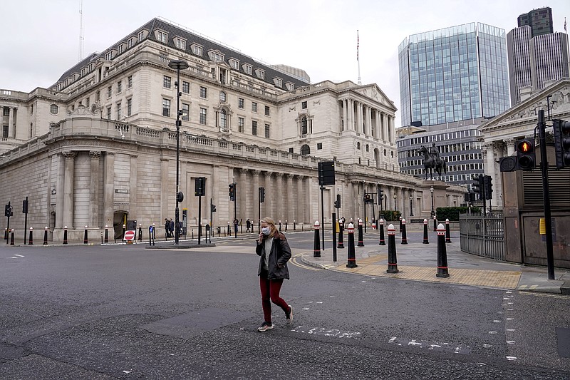 A woman wears a face mask while walking crossing a road outside the Bank of England, in the financial district, known as The City, in London, Monday, Dec. 13, 2021. While many people will re-start working from home, the British government raised the country's official coronavirus threat level on Sunday, warning the rapid spread of omicron &quot;adds additional and rapidly increasing risk to the public and health care services&quot; at a time when COVID-19 is already widespread. (AP Photo/Alberto Pezzali)