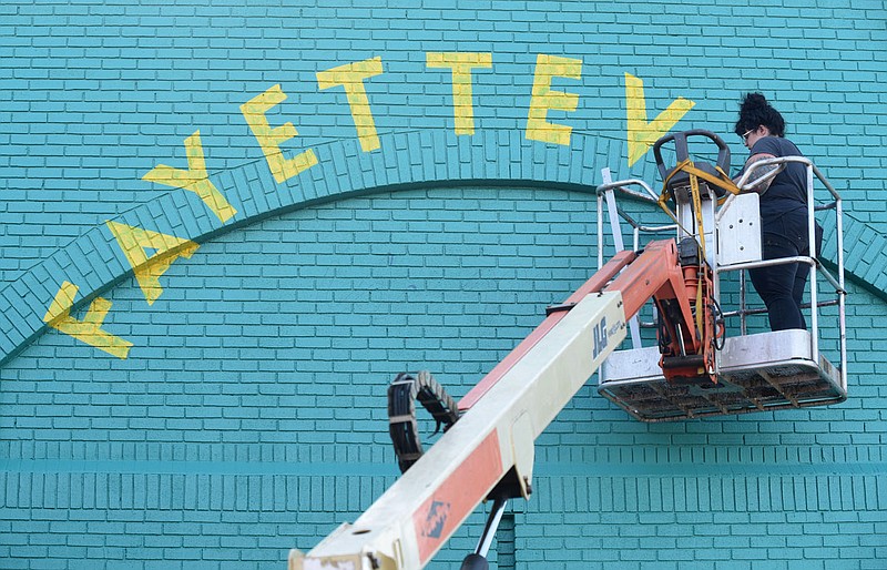 Artist Olivia Trimble, owner of Sleet City Signs and Murals, moves a lift back into position on Aug. 12, 2020, to continue painting a mural on the back side of the Experience Fayetteville building on the square in downtown Fayetteville. The city's Advertising and Promotion Commission on Monday approved its budget for next year.
(File photo/NWA Democrat-Gazette/David Gottschalk)