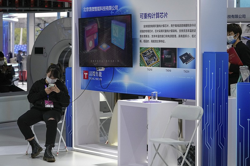A woman wearing a face mask browses her smartphone at a booth displaying various chips developed by Beijing's Tsing Micro at the China Beijing International High-Tech Expo in Beijing on Sept. 26, 2021. Chips are a top priority in the ruling Communist Party's marathon campaign to end China's reliance on technology from the United States, Japan and other suppliers Beijing sees as potential economic and strategic rivals. If it succeeds, business and political leaders warn that might slow down innovation, disrupt global trade and make the world poorer. (AP Photo/Andy Wong)