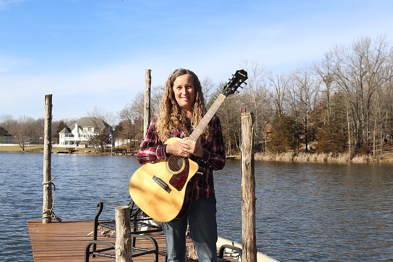 Jan Syrigos holds her guitar on a dock outside her home in Holts Summit.