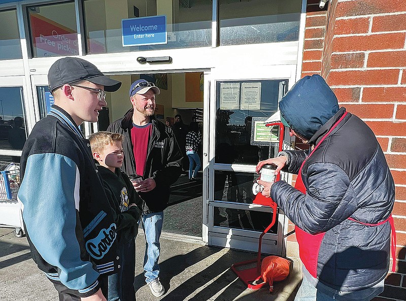 Adam Van Der Hoeven and his two sons Carter Van Der Hoeven and Cyler Van Der Hoeven hand Salvation Army volunteer James Weber a hot coffee on Tuesday, Dec. 21, 2021, at the Police Department in downtown Cheyenne, Wyo. Carter, Cyler and their dad, Adam, have been working to do 25 acts of kindness during the month of December in honor of their late mother and wife who passed away earlier this year. (Rhianna Gelhart/The Wyoming Tribune Eagle via AP)