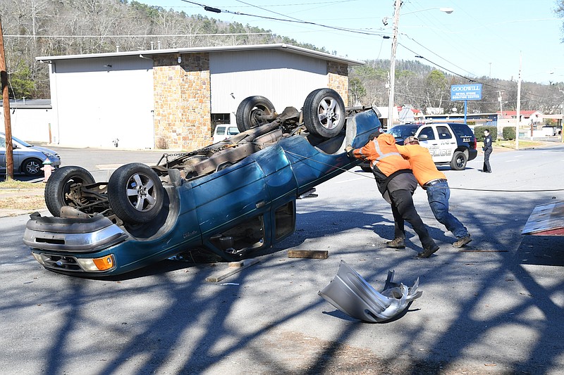 Personnel from A1 Turner Towing and a bystander work to flip a pickup truck back over after a collision shortly before 12:30 p.m. Tuesday near the intersection of Grove Street and East Grand Avenue. - Photo by Tanner Newton of The Sentinel-Record