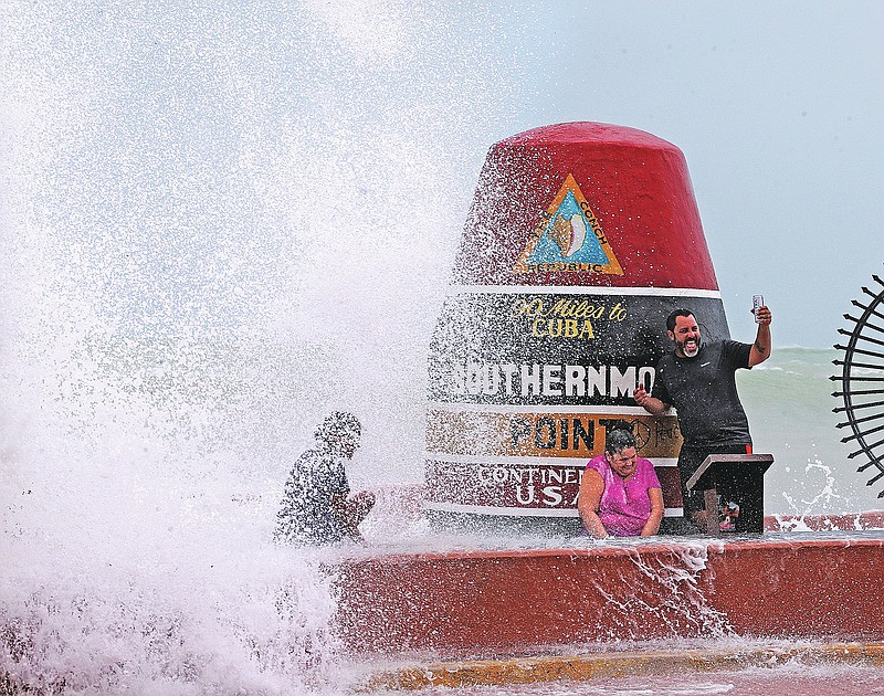 FILE- Key West resident Pedro Lara takes a selfie in front of the Southernmost Point as waves from Hurricane Irma crash over the wall on Sept. 9, 2017.  The 20-ton concrete buoy, which marks the Southernmost Point and 90 miles to Cuba, is one of Key West&#x2019;s famous landmarks. Tourists flock to the marker every day to take photos, snap selfies, buy a souvenir or two.(Miami Herald, Charles Trainor Jr. via AP, File)