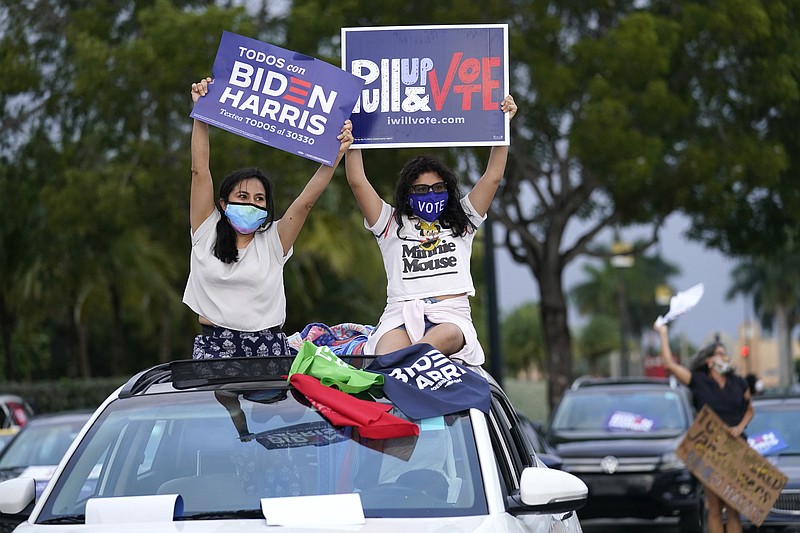 FILE - Claudia Cedillos, left, waves signs with her daughter Montserrat before a campaign rally for Democratic presidential candidate former Vice President Joe Biden, on Nov. 2, 2020, in Miami. Just over a year ago, millions of energized young people, women, voters of color and independents joined forces to send Joe Biden to the White House. But 12 months after he entered the Oval Office, many describe a coalition in crisis. (AP Photo/Lynne Sladky, File)