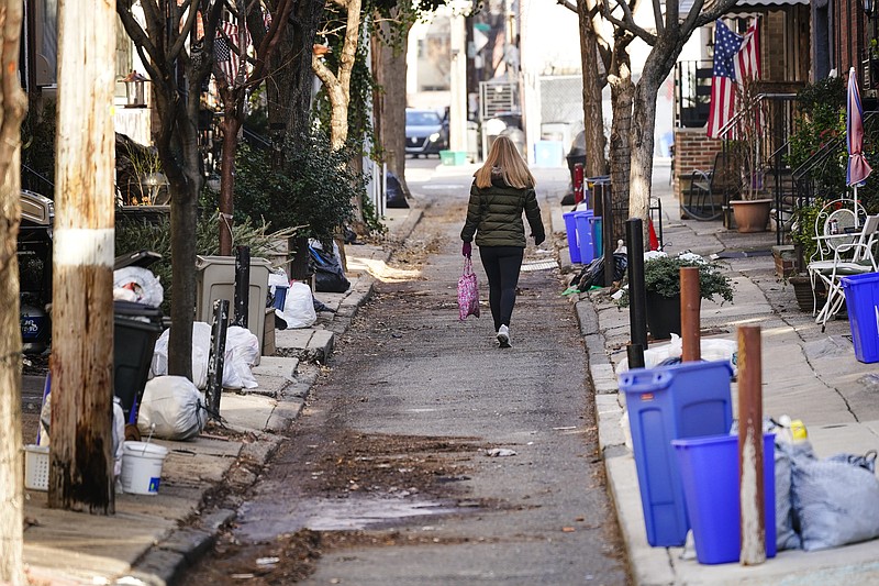 A woman walks past trash waiting for collection Thursday in Philadelphia, Thursday, Jan. 13, 2022. The omicron variant is sickening so many sanitation workers around the U.S. that waste collection in Philadelphia and other cities has been delayed or suspended. (AP Photo/Matt Rourke)