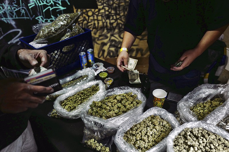 FILE - In this April 15, 2019, file photo, a vendor makes change for a marijuana customer at a cannabis marketplace in Los Angeles. An unwelcome trend is emerging in California, as the nation's most populous state enters its fifth year of broad legal marijuana sales. Industry experts say a growing number of license holders are secretly operating in the illegal market &#x2014; working both sides of the economy to make ends meet. (AP Photo/Richard Vogel, File)