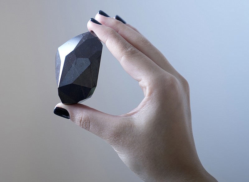 An employee of Sotheby's Dubai presents a 555.55 Carat Black Diamond &quot;The Enigma&quot; to be auctioned at Sotheby's Dubai gallery, in Dubai, United Arab Emirates, Monday, Jan. 17, 2022. (AP Photo/Kamran Jebreili)