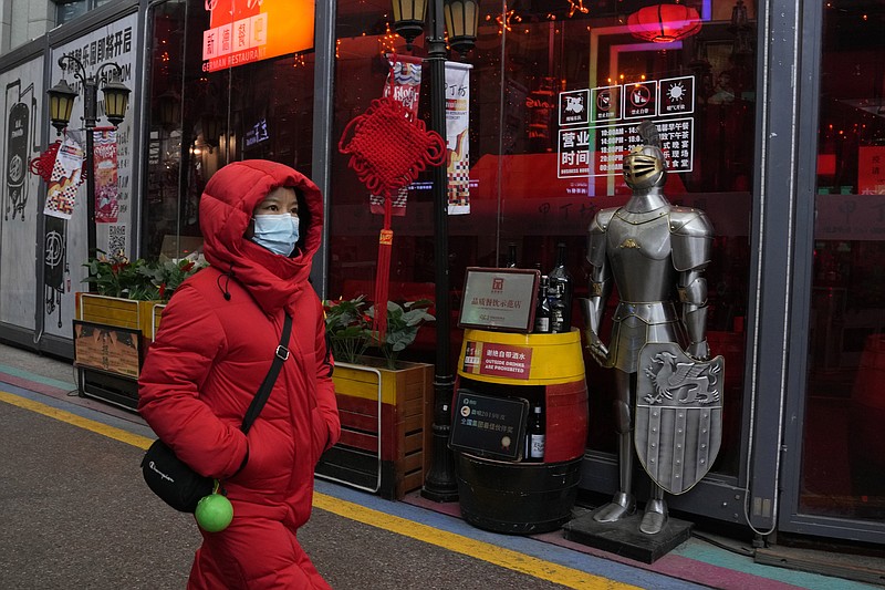 A woman wearing a mask to protect from the coronavirus walks past a coat of armour displayed outside a restaurant in Beijing, China, Friday, Jan. 21, 2022. The sweeping &quot;zero-tolerance&quot; policies that China has employed to protect its people and economy from COVID-19 may, paradoxically, make it harder for the country to exit the pandemic. (AP Photo/Ng Han Guan)