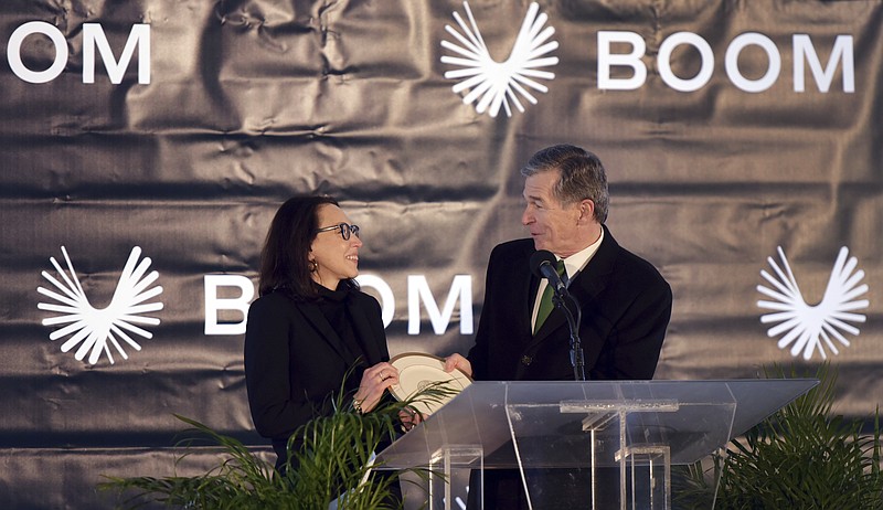 North Carolina Gov. Roy Cooper presents a gift to Kathy Savitt, President and Chief Business Officer of Boom Supersonic, during an announcement, Wednesday, Jan. 26, 2022 that the aviation company will build its supersonic jet at Piedmont Triad International Airport in Greensboro, N.C. The company said it will employ more than 1700 people by the end of the decade. (Walt Unks/Winston-Salem Journal via AP)