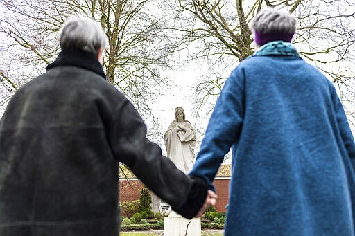 Monika Schmelter, left, and Marie Kortenbusch, right, stand hand in hand in front of a statue of Mary at a convent in Luedinghausen, Germany, Monday, Jan. 24, 2022. More than 100 employees of the Catholic Church in Germany publicly outed themselves as queer on Monday, saying they want to &#x201c;live openly without fear&quot; in the church and pushing demands for it to allow the blessing of same-sex couples and change its labor rules. (Guido Kirchner/dpa via AP)