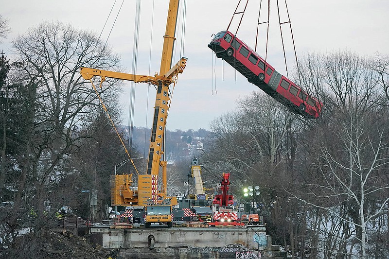Cranes lift the bus that was on a bridge when it collapsed Friday during the recovery process on Monday Jan. 31, 2022 in Pittsburgh's East End. (AP Photo/Gene J. Puskar)
