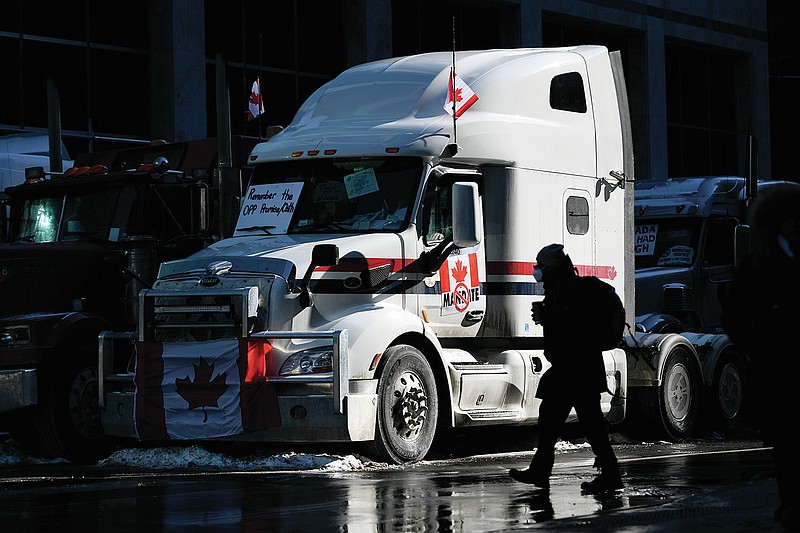 A pedestrian crosses the street near a big rig parked on Metcalfe Street as a protest against COVID-19 restrictions that has been marked by gridlock and the sound of truck horns continues into its second week in Ottawa on Monday, Feb. 7, 2022. (Justin Tang/The Canadian Press via AP)