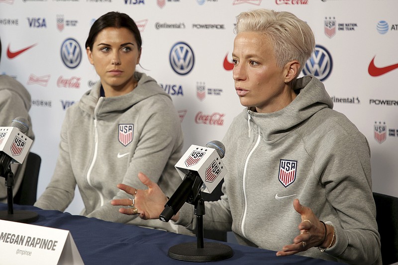 FILE - United States women's national soccer team members Alex Morgan, left, listens as teammate Megan Rapinoe speak to reporters during a news conference in New York, Friday, May 24, 2019. U.S. women soccer players reached a landmark agreement with the sport’s American governing body to end a six-year legal battle over equal pay, a deal in which they are promised $24 million plus bonuses that match those of the men. The U.S. Soccer Federation and the women announced a deal Tuesday, Feb. 22, 2022, that will have players split $22 million, about one-third of what they had sought in damages. (AP Photo/Seth Wenig, File)