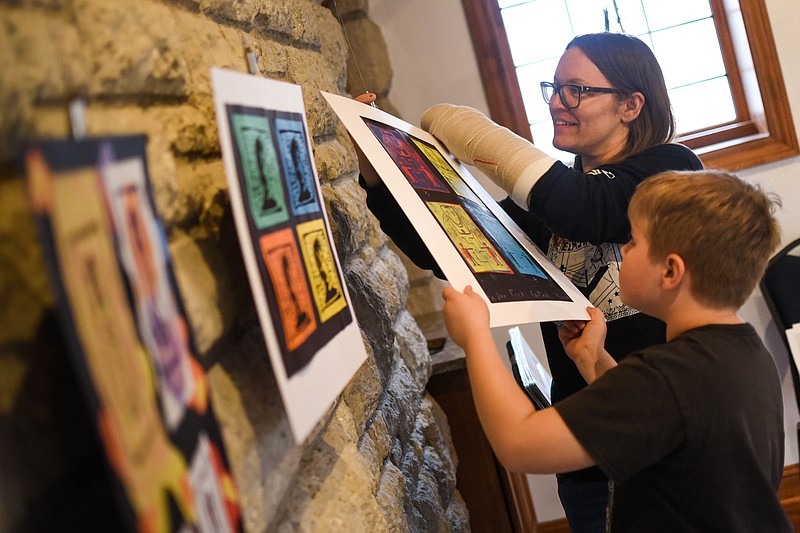 Capital Arts executive director Sarah Scheffer hangs up pieces Wednesday with the help of her son, William, 8, for the “Emerging Artists Exhibition,” which starts March 31 at Capital Arts. (India Garrish/News Tribune)