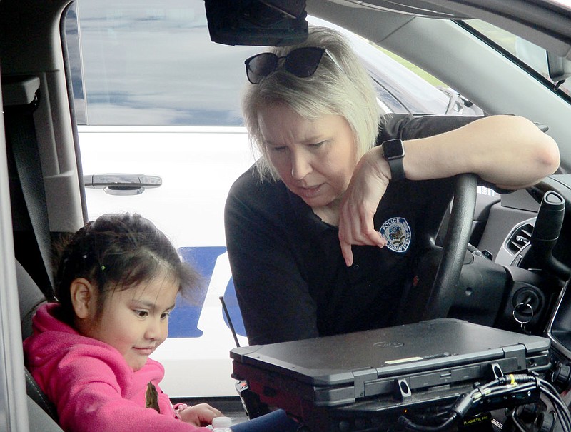 Marc Hayot/Herald-Leader Officer DeAndra Strickland (right), shows Sofia Giron different features on one of the police vehicles on Kite Day which was held Saturday at Siloam Springs Municipal Airport. Giron got to flash the lights and sirens on the police vehicle.