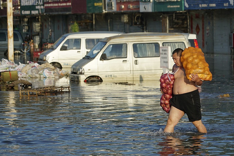 FILE - A man carries bags of onions on a flooded street in Xinxiang in central China's Henan Province Monday, July 26, 2021. A United Nation-backed panel plans to release a highly anticipated scientific report on Monday, April 4, 2022, on international efforts to curb climate change before global temperatures reach dangerous levels.(AP Photo/Dake Kang, File)