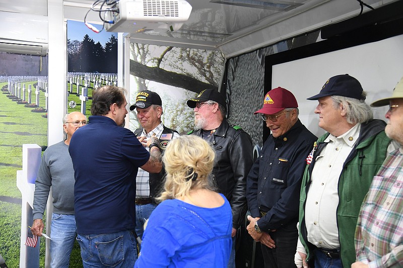 Stefan Brann, left, and Jennifer Merrill, foreground, ambassadors for Wreaths Across America, present lapel pins to Vietnam and Vietnam-era veterans who stopped by the Wreaths Across America mobile education exhibit on Friday. - Photo by Tanner Newton of The Sentinel-Record