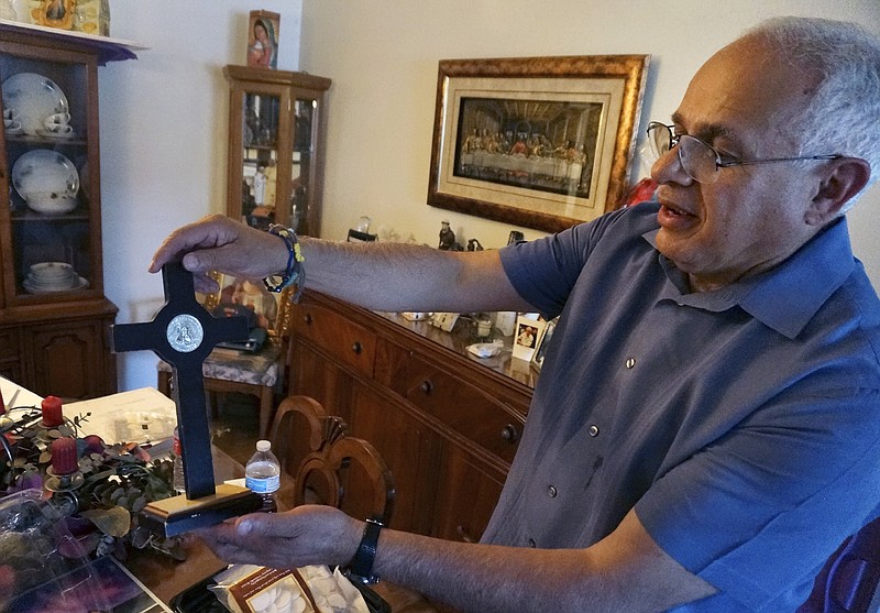 Bob Guerra, a Catholic deacon, holds a crucifix he got to commemorate the visit of Pope Francis to the U.S.-Mexican border at his house in El Paso, Texas, on Sunday, April 3, 2022. Guerra takes the crucifix alongside other liturgical items to help clergy celebrate Mass for hundreds of teens held at a shelter on the Army's Fort Bliss base after crossing the border without parents or guardians. (AP Photo/Giovanna Dell'Orto)