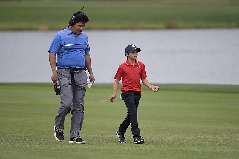 FILE - Golf Channel and NBC on-course analyst Notah Begay, left, talks with Charlie Woods, son of golfer Tiger Woods, as they walk on the 18th fairway analyst during the final round of the PNC Championship golf tournament, Sunday, Dec. 20, 2020, in Orlando, Fla. Notah Begay III is competing in a tournament for the first time in nearly 10 years, and the score isn’t what matters to him. His appearance on the Advocates Professional Golf Association Tour in Arizona has been a mixture of inspiration and appreciation. (AP Photo/Phelan M. Ebenhack, File)