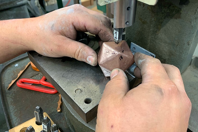 Woody Maringer uses a punch Friday, April 15, 2022, to stamp numbers onto the sides of a solid copper 20-sided die at Shire Post Mint in West Fork. The company has garnered a lot of attention for the products and for the videos of the items? casting on social media. Visit nwaonline.com/220424Daily/ for today's photo gallery. 
(NWA Democrat-Gazette/Andy Shupe)