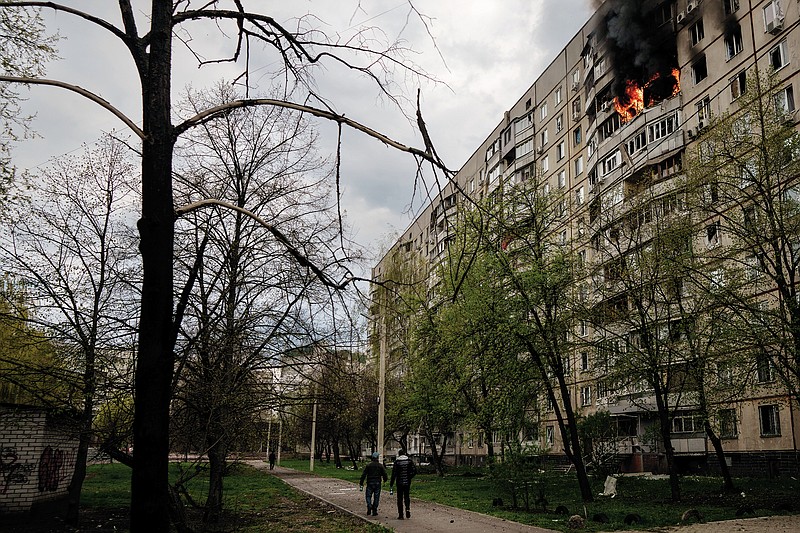 People walk near an apartment on fire after it was hit during a Russian bombardment in Kharkiv, Ukraine, Friday, April 22, 2022. (AP Photo/Felipe Dana)