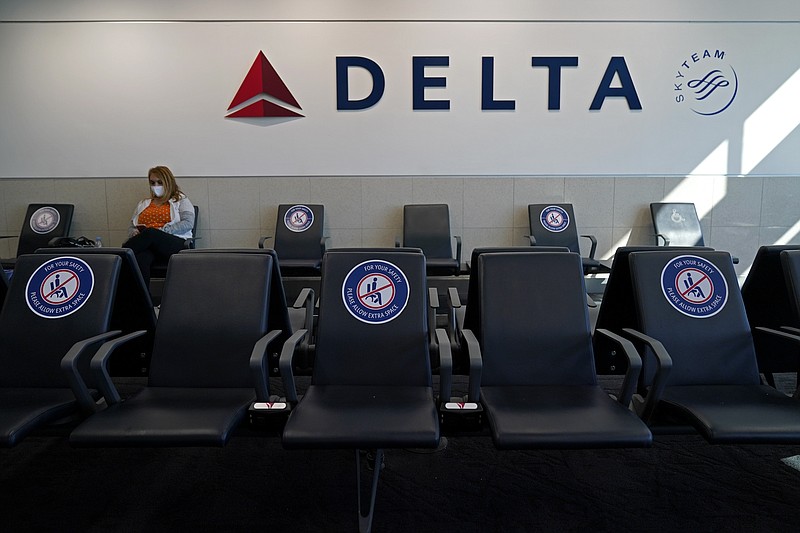 A passenger wears a face mask as she waits in a socially-distance area for a Delta Airlines flight, Wednesday, Feb. 3, 2021, at Hartsfield-Jackson International Airport in Atlanta.  Delta Air Lines will start paying flight attendants during the time that passengers are boarding. That's a first for a major U.S. airline. Flight attendants in the U.S. generally don't begin getting paid until the doors close after boarding. Delta said Tuesday, April 26, 2022, that the change will take effect in June, and it comes on top of pay raises for flight attendants. The pay increase comes as Delta faces another attempt by unions to organize its non-union flight attendants.  (AP Photo/Charlie Riedel, File)
