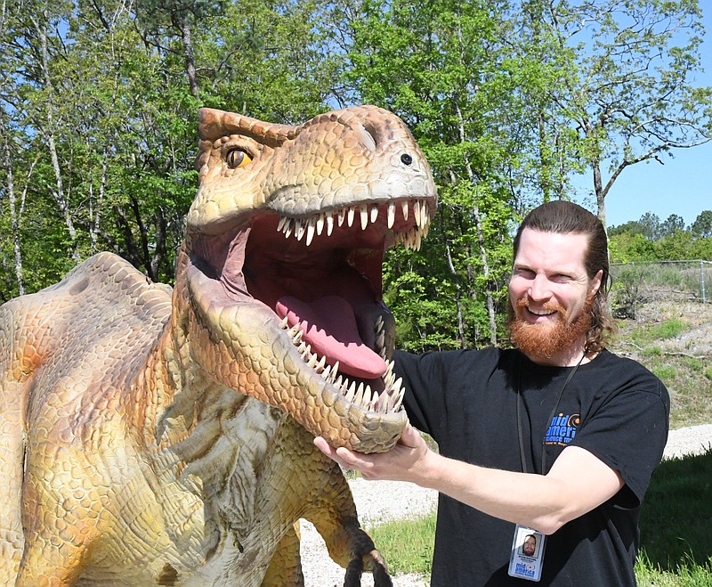 Dylan Kuchel, director of buildings, grounds and facilities, with Tee Wrexx, one of the dinosaurs found along the Oaklawn Foundation DinoTrek at Mid-America Science Museum. - Photo by Tanner Newton of The Sentinel-Record
