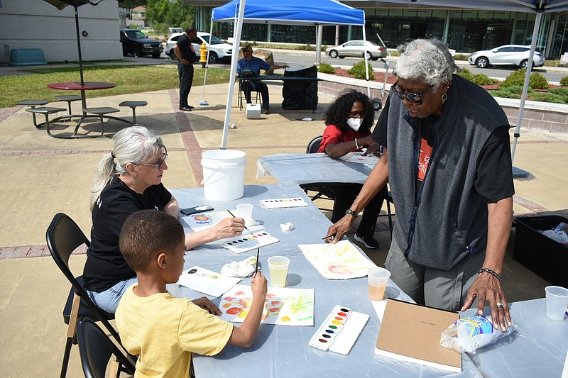 Artist Scinthya Edwards shows Zion Reed, 5, some painting techniques as Zion's play-grandmother, Betty Brown (left), and Denita Wright (background) do their own paintings at the UAPB Art Experience in downtown Pine Bluff on Saturday, April 30, 2022. (Pine Bluff Commercial/I.C. Murrell)