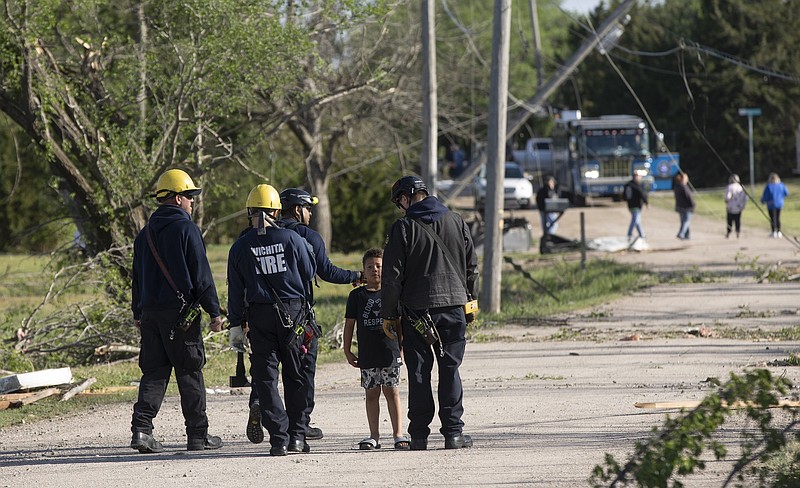 Wichita firefighters fist-bump 7-year-old Camden Oyewole while searching an area in Andover, Kan., on Saturday, April 30, 2022. A suspected tornado that barreled through parts of Kansas has damaged multiple buildings, injured several people and left more than 6,500 people without power. (Jaime Green /The Wichita Eagle via AP)
