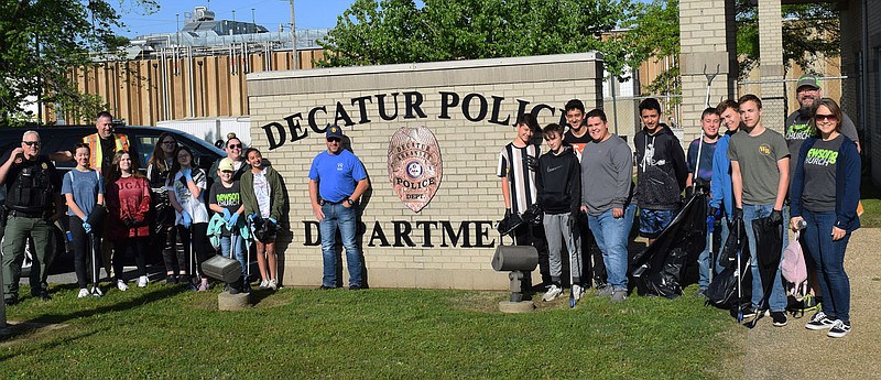 Westside Eagle Observer/MIKE ECKELS The Newsong youth group and advisers pose with members of the Decatur Police Department in front of the station house in Decatur on May 7. Shortly after this moment, the church group began picking up trash along both Arkansas highways 59 and 102 to the Decatur city limits.