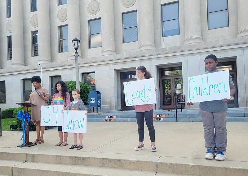 Veronica Smith-Creer describes the need for foster families in Union County while, from left to right, Carmen Bennett, John-Luke Bennett, Lily Langston and Lyric Brown hold signs highlighting key statistics. (Courtesy of Karen Hicks/Special to the News-Times)