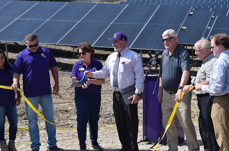 Fountain Lake School District Superintendent Michael Murphy and school board President Dana Greeson hold the scissors during Monday’s ribbon-cutting ceremony for the new solar power plant, as solar modules are seen from behind. - Photo by Donald Cross of The Sentinel-Record
