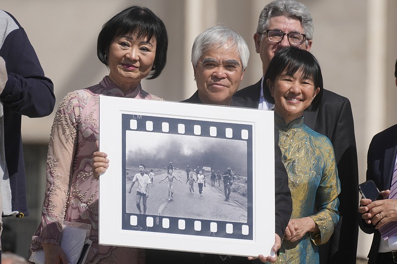 Nick Ut, center, flanked by Kim Phuc, left, holds the "Napalm Girl", his Pulitzer Prize winning photo as they wait to meet with Pope Francis during the weekly general audience in St. Peter's Square at The Vatican, Wednesday, May 11, 2022. Ut and UNESCO Ambassador Kim Phuc are in Italy to promote the photo exhibition "From Hell to Hollywood" resuming Ut's 51 years of work at the Associated Press, including the 1973 Pulitzer-winning photo of Kim Phuc fleeing her village after it was accidentally hit by napalm bombs dropped by South Vietnamese forces. (AP Photo/Gregorio Borgia)