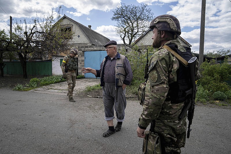 A Ukrainian serviceman talks with a local resident after de-mining the residential area after shelling of Russian forces in Maksymilyanivka, Ukraine, Tuesday, May 10, 2022. (AP Photo/Evgeniy Maloletka)