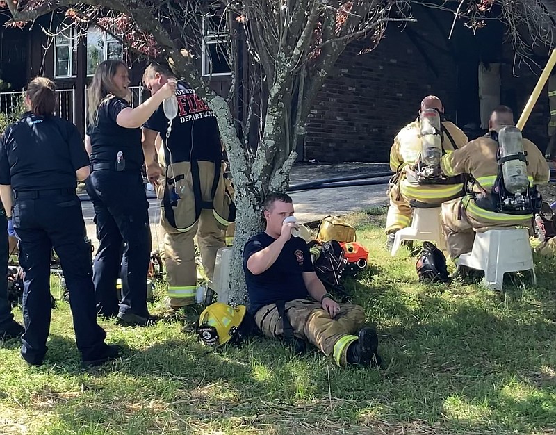 A Hot Springs firefighter receives an IV while another leans against a tree and drinks water during a house fire at 215 Television Road on Wednesday. - Photo by Tanner Newton of The Sentinel-Record